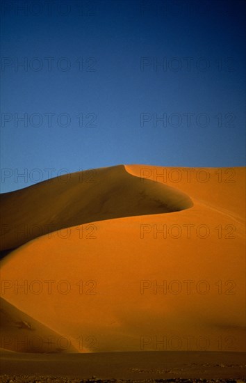 LIBYA , South West, Achan , Orange desert sand dune against a clear blue sky