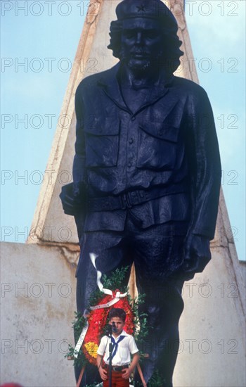 CUBA, Holguin Province, Moa, Young child at memorial day with statue of Che Guevara behind.