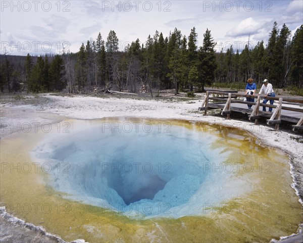 USA, Wyoming, Yellowstone, People looking into Morning Glory hot pool in the National Park.  Ochre and turquoise rock