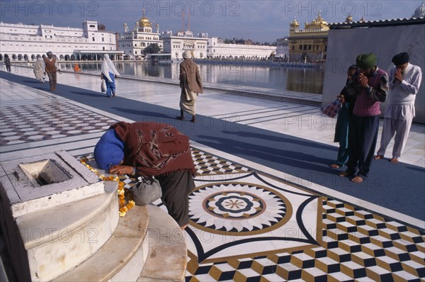 INDIA, Punjab, Amritsar, Barefooted pilgrims saying prayers at Golden Temple complex with offering of marigold flower garland lying on marble step.