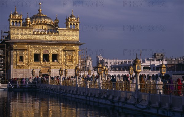 INDIA, Punjab, Amritsar, Pilgrims on causeway known as the Guru’s Bridge leading to the Golden Temple reflected in rippled surface of pool below.
