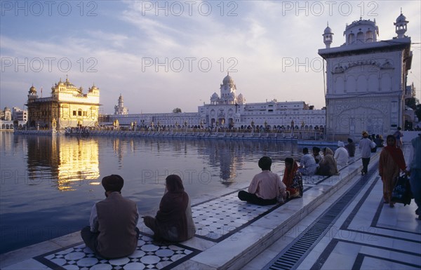 INDIA, Punjab, Amritsar, Golden Temple with pilgrims in low light with shimmering temple reflected in water of sacred pool.
