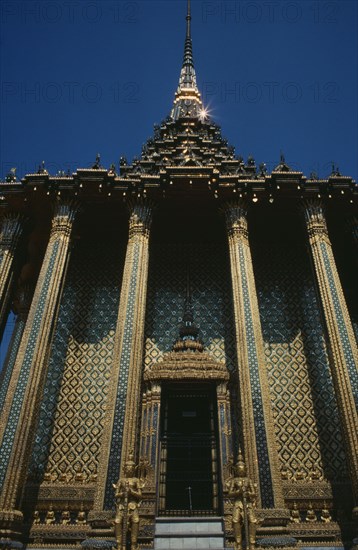 THAILAND, Bangkok, Grand Palace, Wat Phra Kaeo. View looking up at golden facade columned entrance and statues