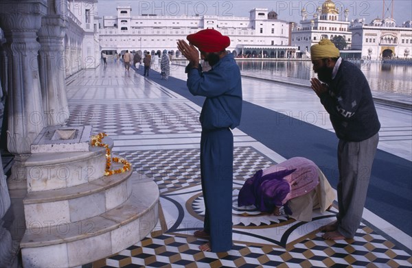 INDIA, Punjab, Amritsar , Pilgrims praying at shrine in the Golden Temple with garland of marigold flowers laid over marble steps.