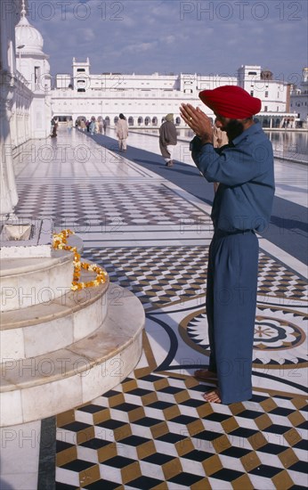 INDIA, Punjab, Amritsar, Golden Temple.  Barefooted Sikh man praying in front of shrine with garland of marigold flowers lying across marble steps.