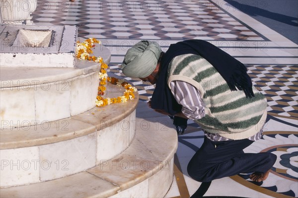 INDIA, Punjab, Amrtisar , Golden Temple.  Barefoot Sikh pilgrim kneeling at shrine to pray with garland of marigold flowers laid out on marble steps.