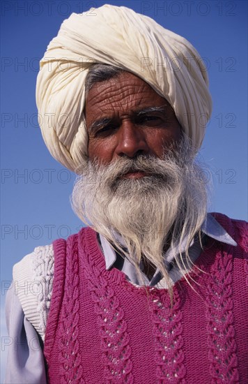 INDIA, Punjab, Amritsar , "Elderly bearded Sikh man, head and shoulders portrait wearing white turban and pink knitted tank top."