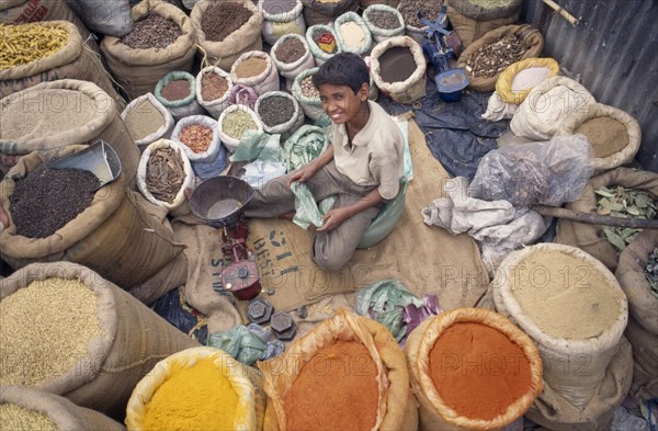 INDIA, Delhi , Spice market, View looking down on young vendor sitting at scales in the middle of sacks of spices