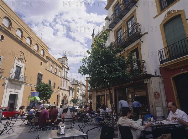 SPAIN, Andalucia, Seville, "Santa Cruz District, Calle Santa Maria la Blanca with people sitting at tables outside restaurants and bars"