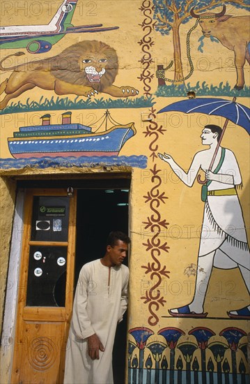 EGYPT,  , Luxor, Man at door of tourist shop decorated with mock hieroglyphics depicting the 20th Century