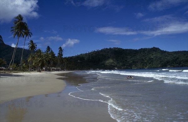 WEST INDIES  , Trinidad, Maracas Bay , Sandy beach with couple lying in the surf and tree covered headland beyond.