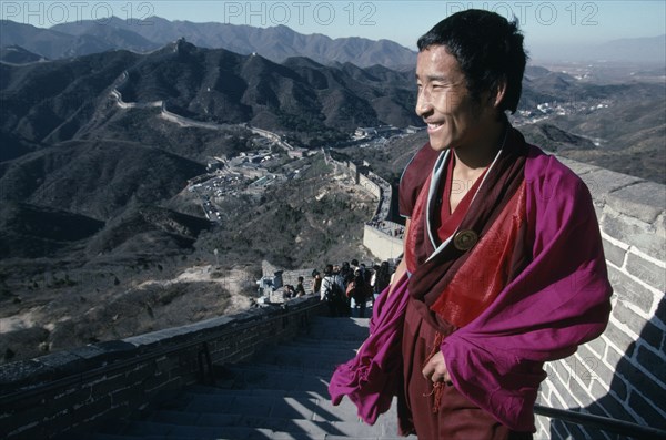 CHINA, Beijing Division, Badaling, Tibetan Monk standing at the top of steps on The Great Wall which spans the hilly landscape beyond