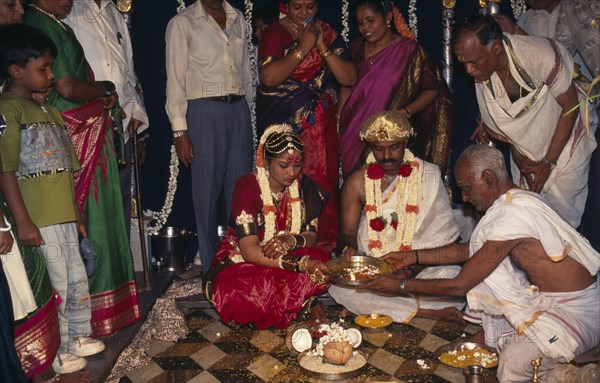 INDIA, Bangalore , Hindu Wedding, People standing around sitting couple wearing traditional wedding dress.