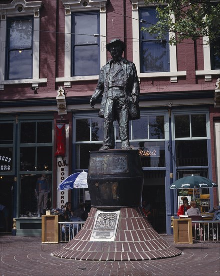 CANADA, British Columbia, Vancouver, Gastown. Bronze statue of Gassy Jack the father of Gastown with a cafe behind
