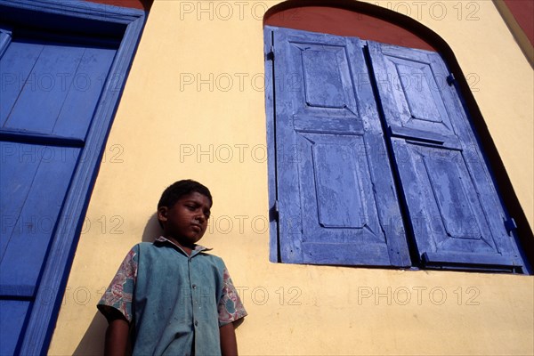 INDIA, Kerala, Kochin , Angled view of a boy standing by a yellow house with a blue door and window shutters