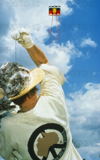 SPORT, Kites, Person flying kite seen from behind at low angle looking up into blue sky with white clouds.