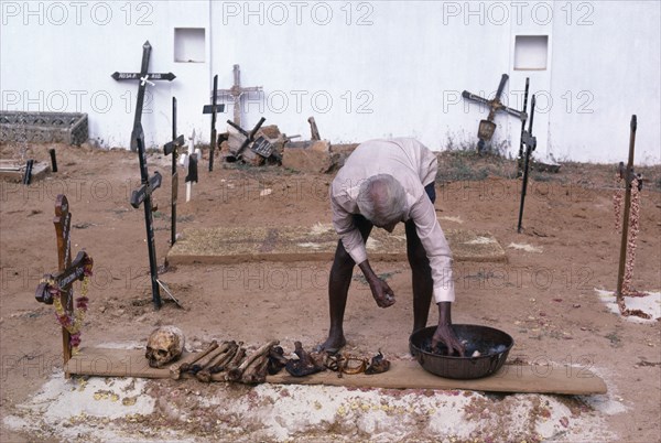 INDIA, Goa , Man in a cemetary cleaning bones that have been removed from a family grave which will be replaced to make room for the next family member