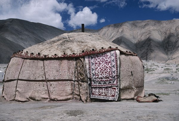 CHINA, Xinjiang, Karakol Lake Area, Khirgiz yurt in barren mountain landscape with decorated textile hanging over door