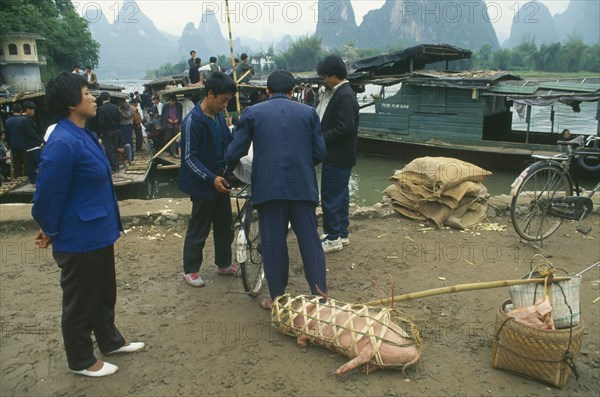 CHINA, Guangxi Province, Guilin , Villagers loading boats after market with pig in basket in the foreground.