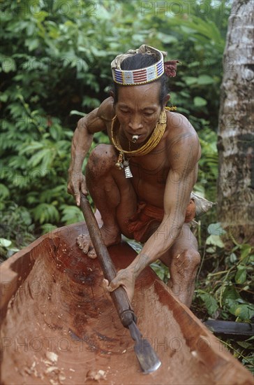 INDONESIA, Sumatra, Siberut Island, A Mentawi man hollowing out a canoe whilst he smokes a hand rolled cigarette