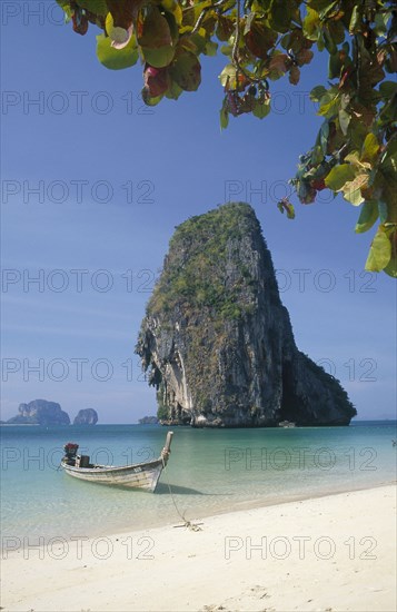 THAILAND, Krabi Province, Phra Nang Beach, Long tail boat in clear calm blue water at the edge of he beach with limestone islands behind