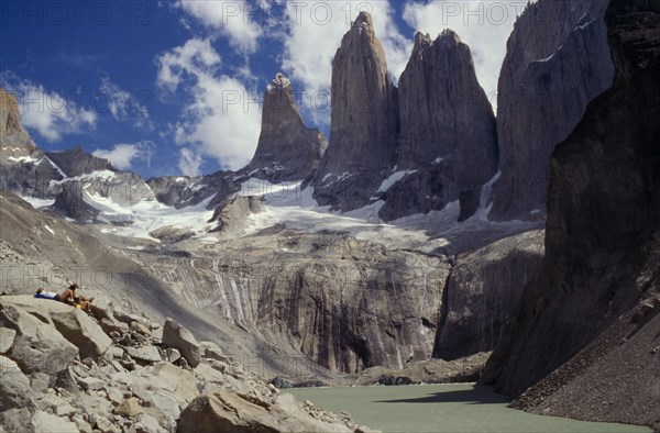 CHILE, Torres Del Paine, Parque Nacional, Hikers resting on hillside above a river and below towering snow capped mountains