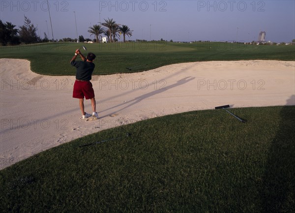 QATAR, Doha, Doha Golf Club.  Male golfer playing out of a bunker on short nine hole floodlit course.