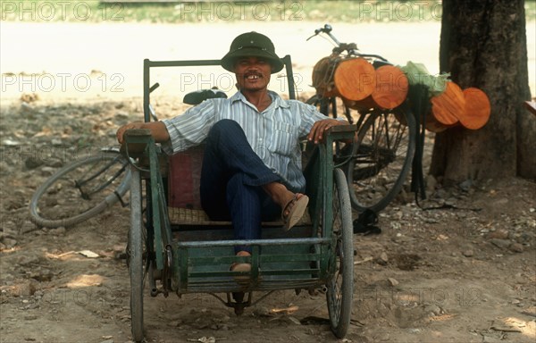 VIETNAM, Hanoi, Cyclo driver sitting in his vehicle under the shade of a tree.