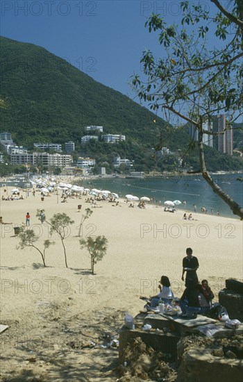 HONG KONG, Discovery Bay , View through tree branches towards golden beach with people on sand and houses built onto the hillside behind