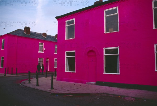 ENGLAND, Greater Manchester , Salford , Terrace houses on Ash Street painted shocking pink with couple standing in the road