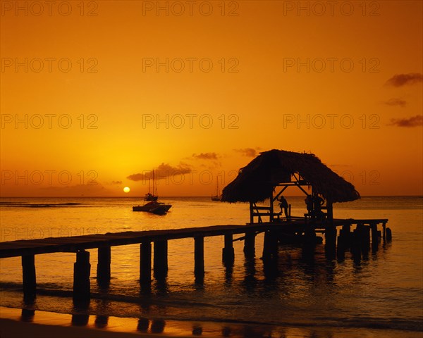 WEST INDIES, Tobago, Pigeon Point, Wooden jet and boat silhouetted at sunset.