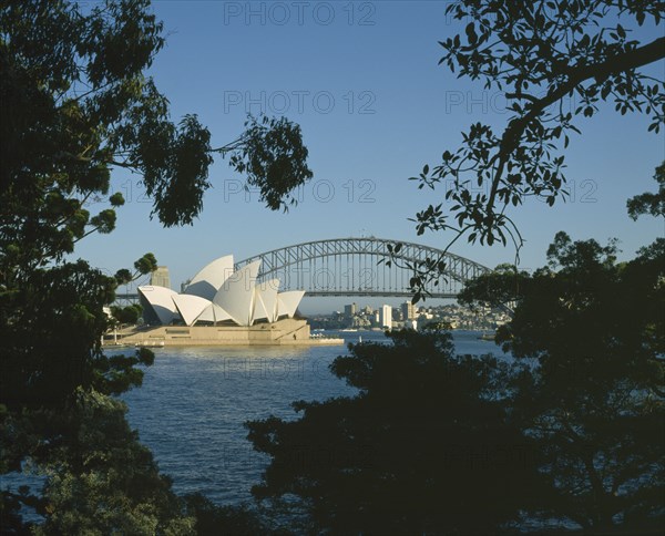 AUSTRALIA, New South Wales, Sydney, Harbour Bridge and Opera House seen through trees from the Royal Botanic Gardens