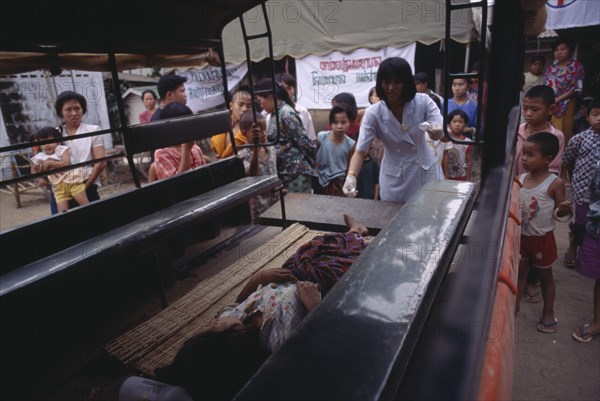 THAILAND, North, Mae Sai, Karen refugee recieving medical attention watched by a crowd of children