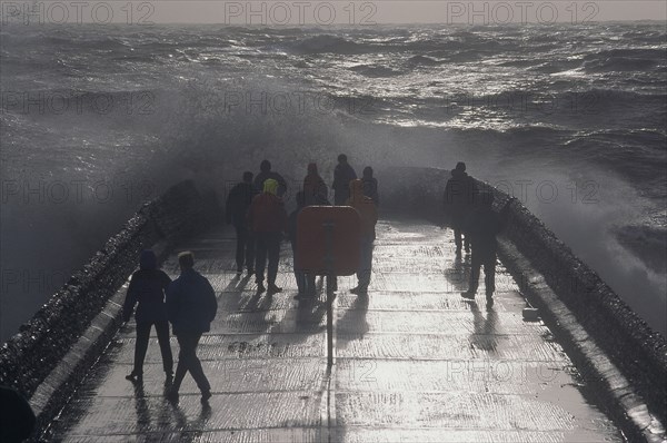 ENGLAND, East Sussex, Brighton, Waves crashing over a groyne with people on it