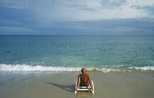 THAILAND, Surat Thani, Koh Samui, Lamai beach with lone male tourist sitting on a sunbed on the empty beach