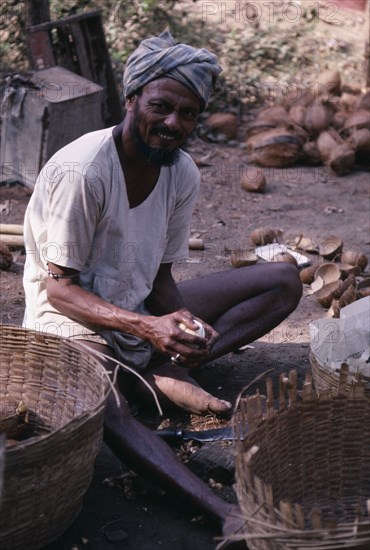 INDIA, Goa, Colva, Copra or coconut worker sitting with baskets and holding shelled coconut