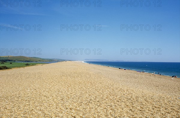 ENGLAND, Dorset, Chesil Beach, The shingle beach and lagoon stretching towards distant horizon with sunbathers along the shoreline.
