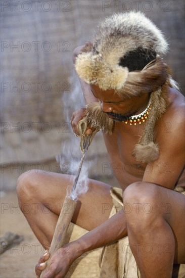 SOUTH AFRICA, KwaZulu-Natal , Eshowe, Zulu man burning hole into shaft to make spear.