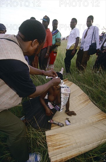 SOUTH AFRICA, KwaZulu Natal , Melmoth, Zulu man pinning money to a girl's head whilst she sits on a mat in a field at a coming of age ceremony.