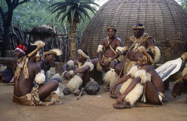 SOUTH AFRICA, KwaZulu Natal, Tribesmen sitting on the ground outside a hut whilst the chief sits on a chair because of his seniority