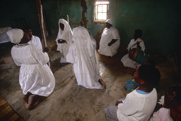 SOUTH AFRICA, KwaZulu Natal, Melmoth, Zulu Zionists women wearing white kneeling on the earth ground inside a house praying