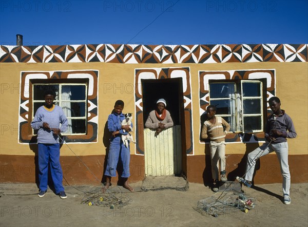 SOUTH AFRICA, Tribal Peoples, Basotho family outside typical painted home. young boys with model toy cars.