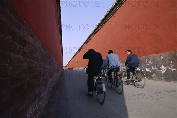 CHINA, Hebei, Beijing, Imperial Palace with cyclists riding down a long red alleyway