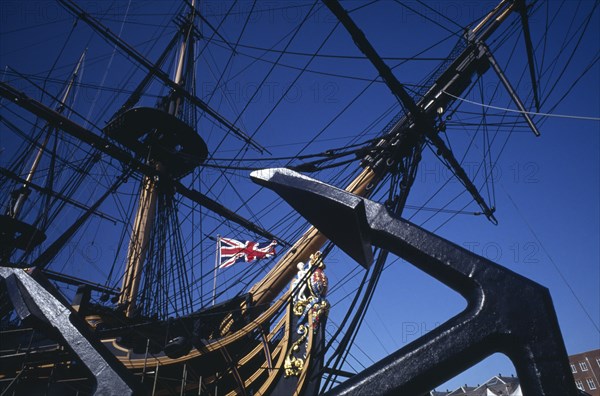 ENGLAND, Hampshire, Portsmouth, Admiral Lord Nelson’s HMS Victory in Portsmouth’s Historic Dockyard.  Angled view of bow of ship with figurehead and Union Jack flag.  Anchor in foreground.
