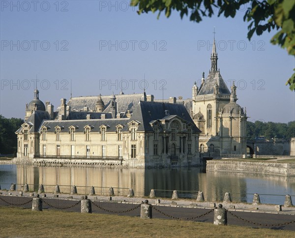 FRANCE, Nord Picardy, Oise, Chantilly Chateau with its reflection in surrounding water and a road in the foreground