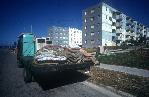 CUBA, Havana , Blocks of flats with truck parked in the foreground and two men carrying furniture down the path