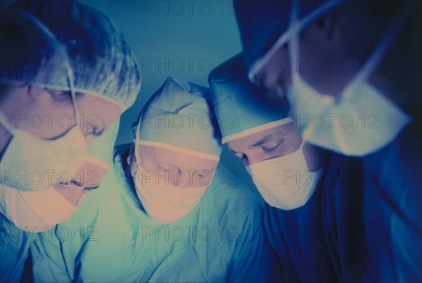 MEDICAL, Doctors, Surgeons, Operating theatre with five medical staff wearing surgical masks looking down towards patient