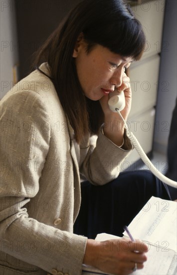 COMMUNICATIONS, Phones, Using, Woman using landline telephone and making notes on paper beside her.