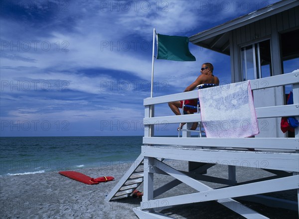 USA, Florida , Sarasota, Lido Beach. Lifeguard man sitting on high stall looking out to sea in Lifeguard Hut with Green Flag