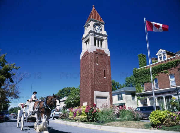 CANADA, Ontario , Niagara on the Lake, Queen Street Clock Tower with Canadian flag flying. Horse and carriage travelling along road